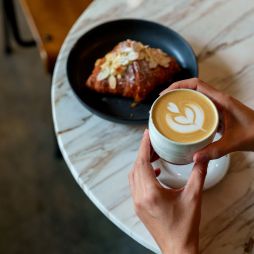 person holiding coffe and croissant in cafe